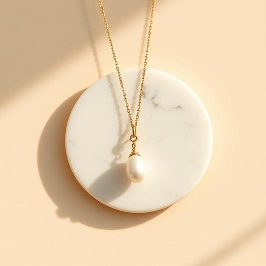 Yellow gold pearl drop pendant on warm marble