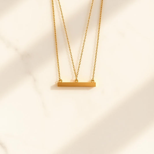 Yellow gold horizon bar pendant on warm marble